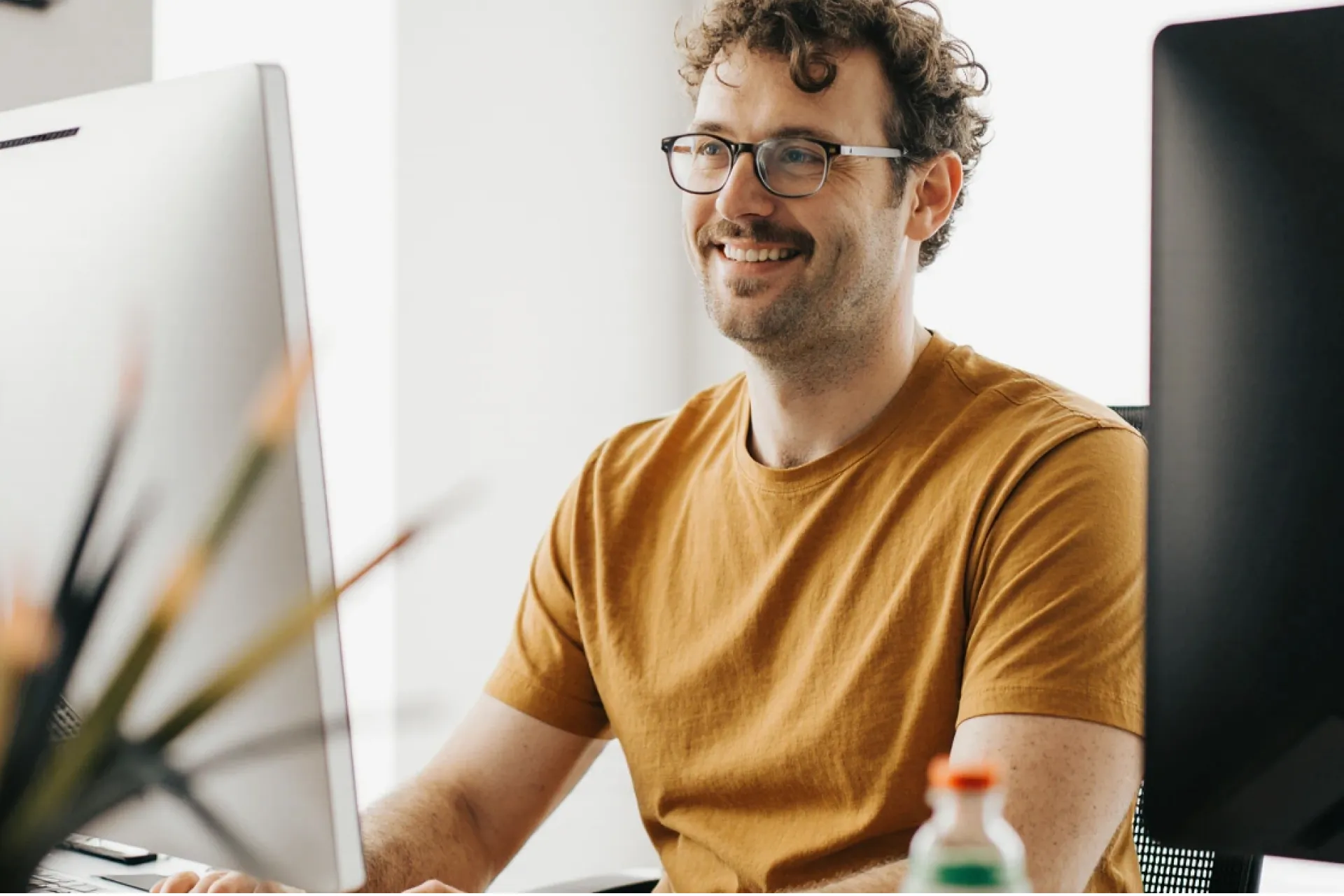 Smiling man at a desk between two computer monitors
