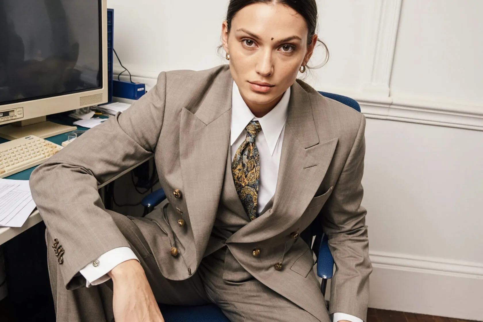 Woman in a tweed suit and tie sitting at an office desk