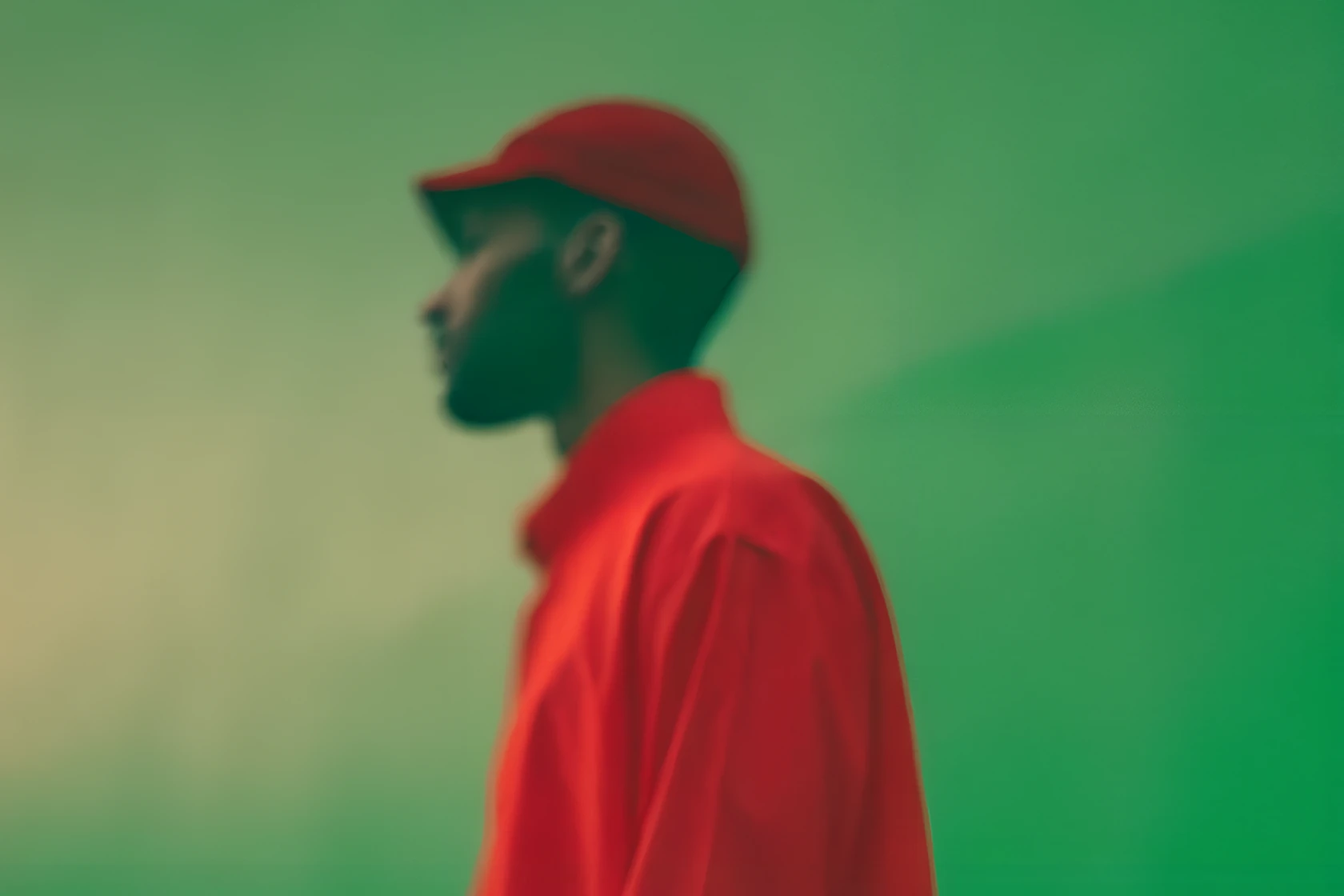 Man in a red cap and jacket in profile against a green wall