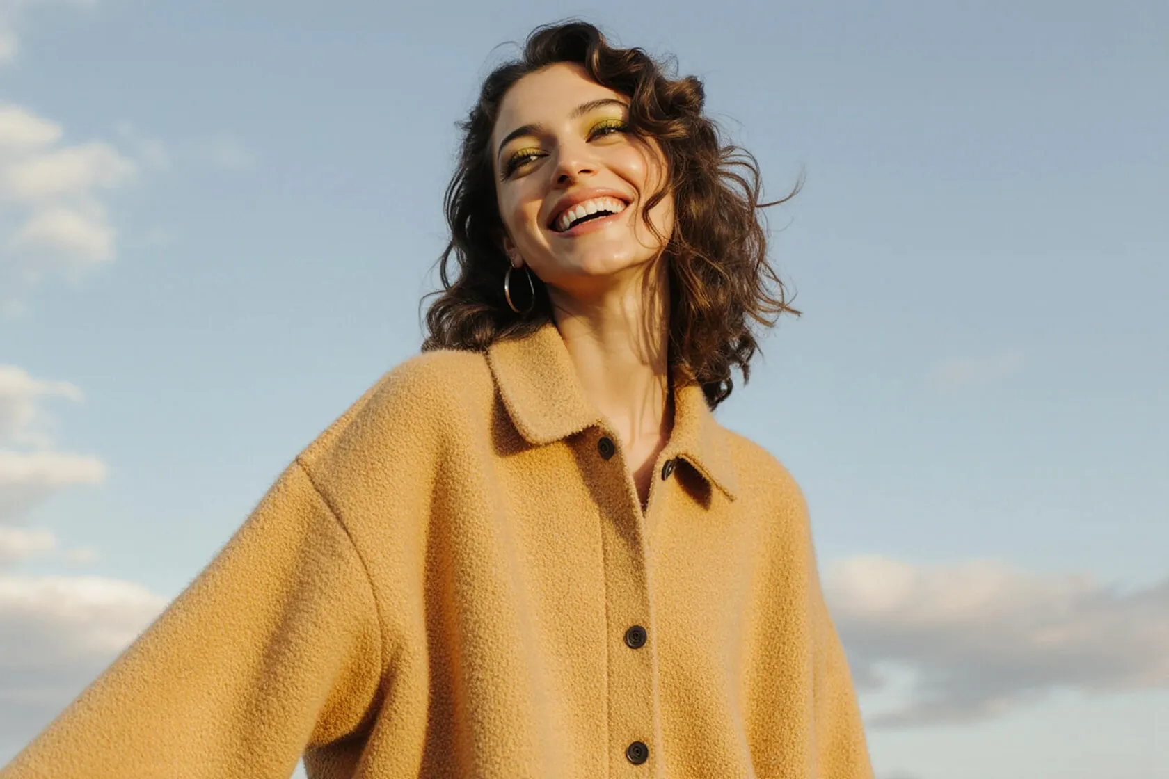 Laughing woman in a mustard coat against the sky