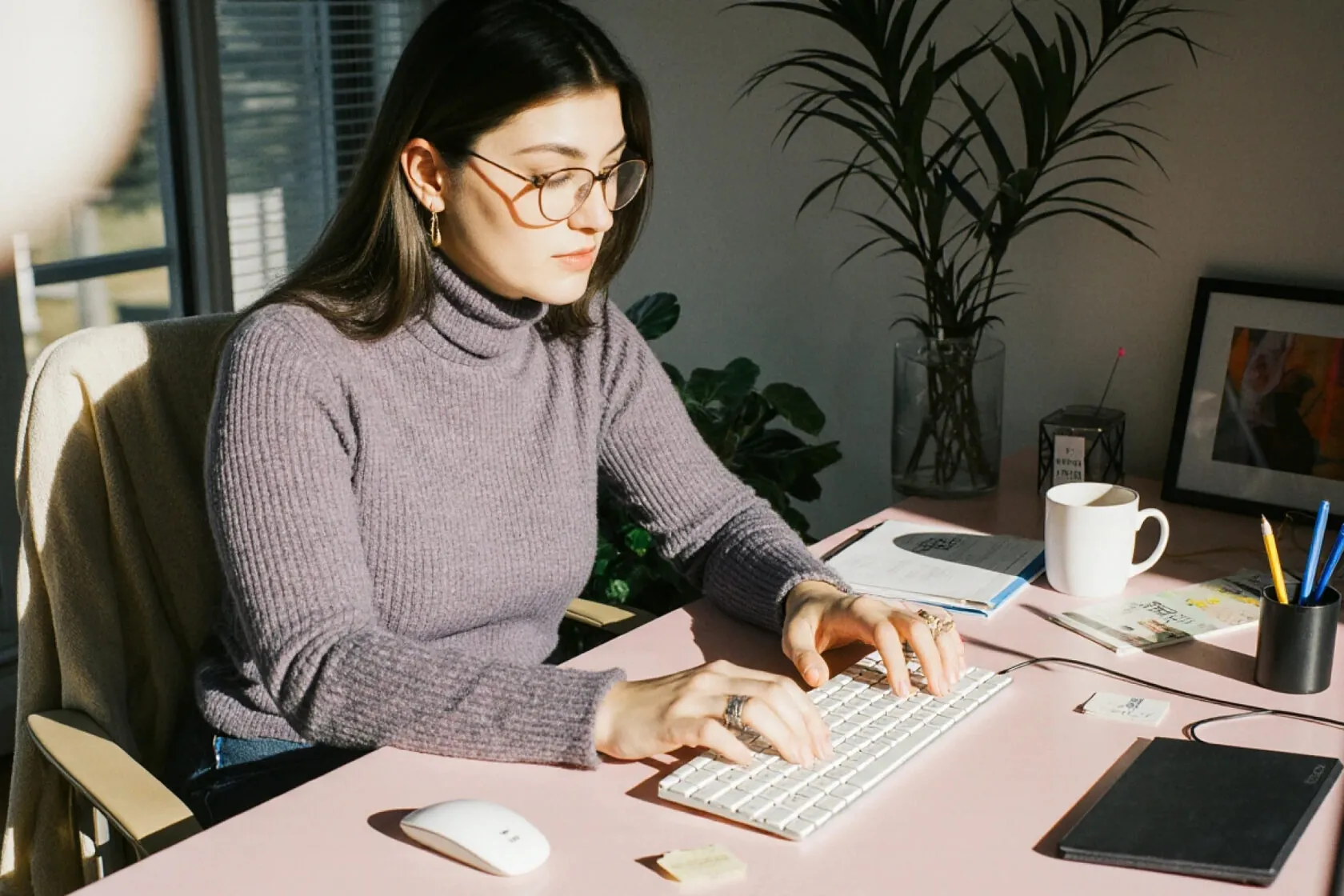 Woman in glasses typing at a desk in a bright home office
