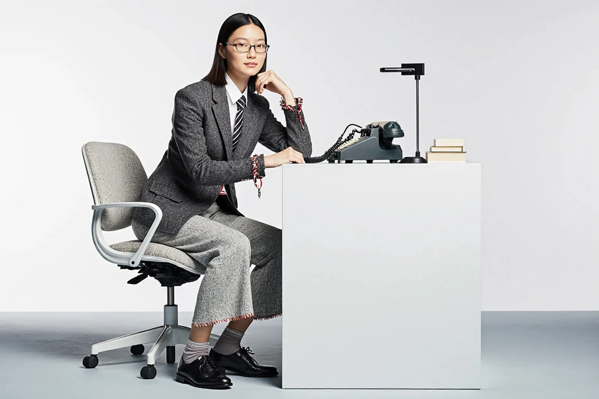 Woman in a grey suit posing at a white desk with a vintage phone